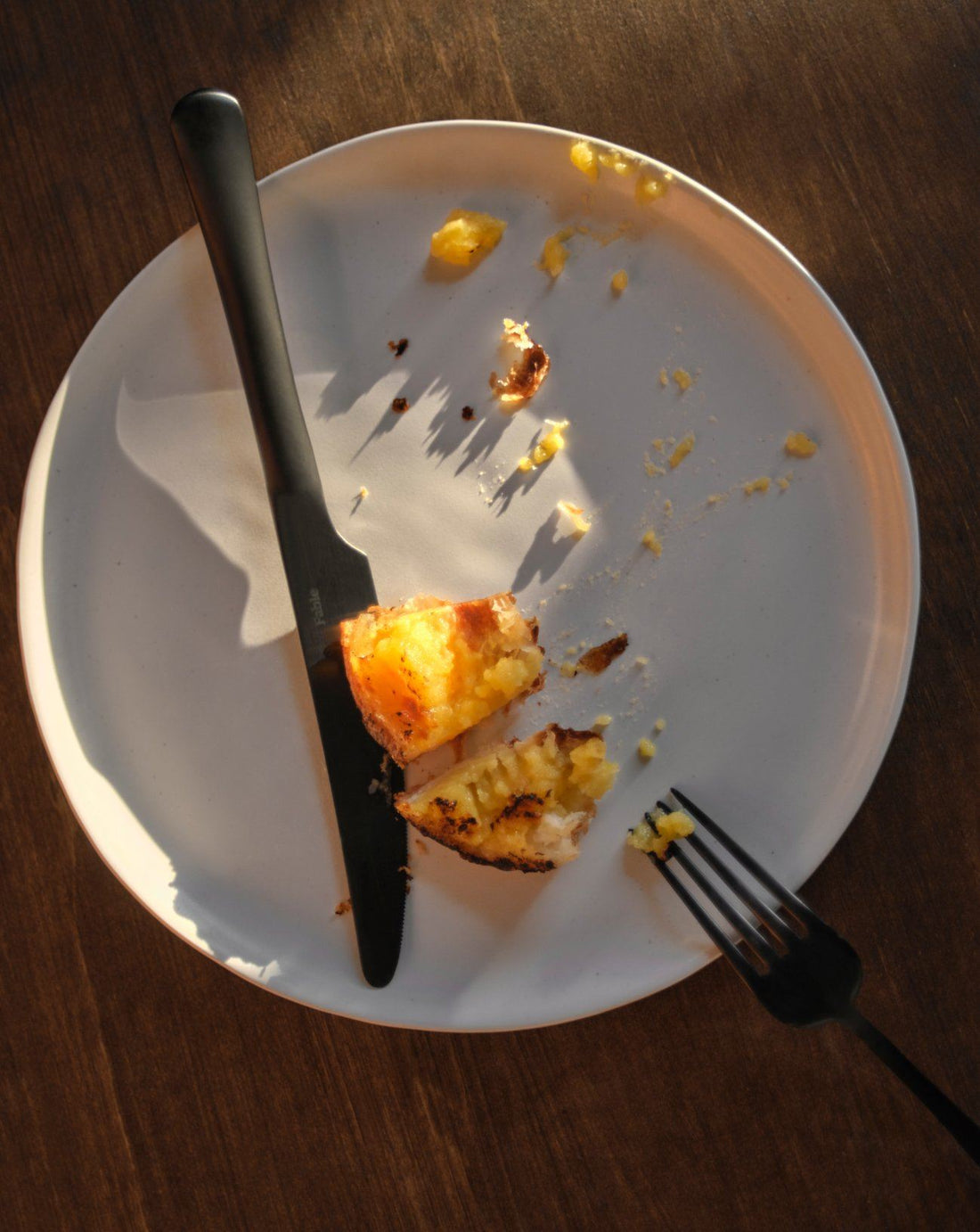 A top-down view of a white plate with remnants of a meal served with a fork and knife. 