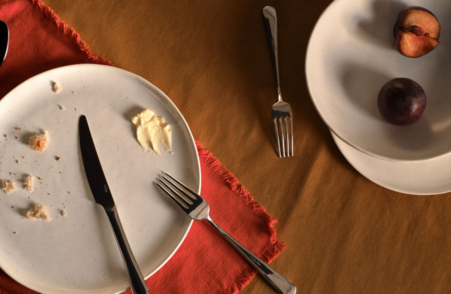 A top-down view of a table, showing a tablecloth, speckled white plates, and silverware.