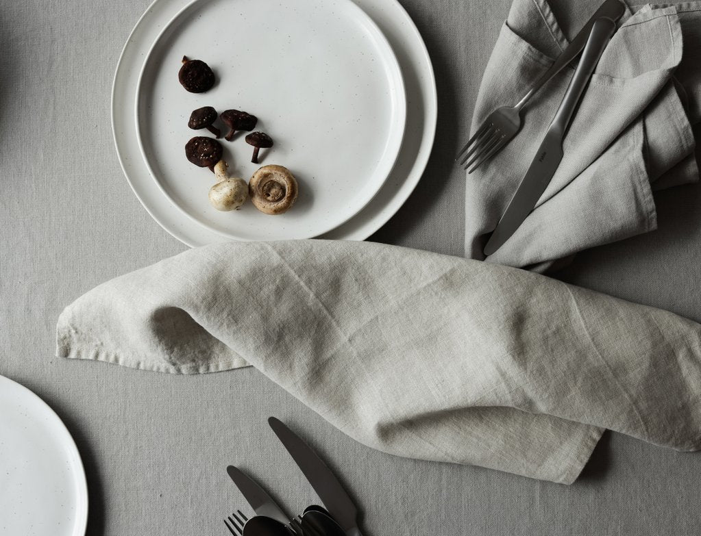 Top-down view of a table with a tablecloth, napkins, silverware, and speckled white plates.
